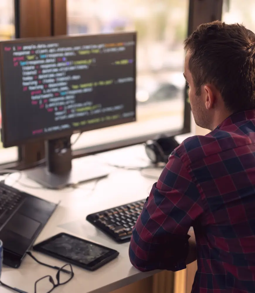 Image of a man sitting at a desk looking at code on a computer screen